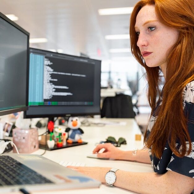 A focused female software engineer coding on dual monitors in a modern office.